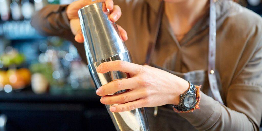 Close up of a person holding a cocktail shaker in a bar