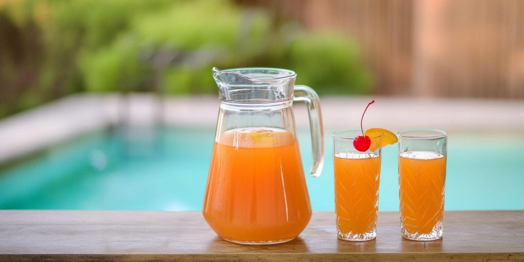 A jug and two glasses of Hurricane cocktail next to a pool in summertime