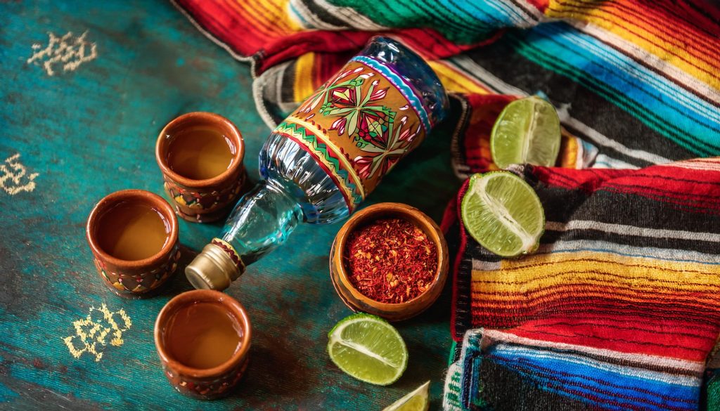 Top view of a selection of gifts for tequila lovers on a colorful fabric backdrop, including a bottle of tequila, interesting salts and more