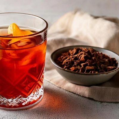 A London Fog cocktail on a textured white surface next to a bowl of cocoa nibs