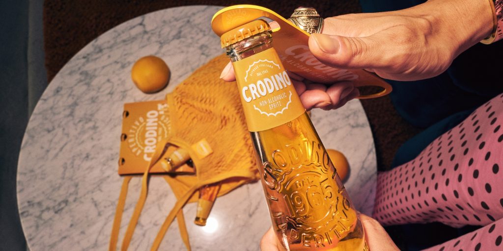 Close-up of a bottle of Crodino being opened with a branded bottle opener 