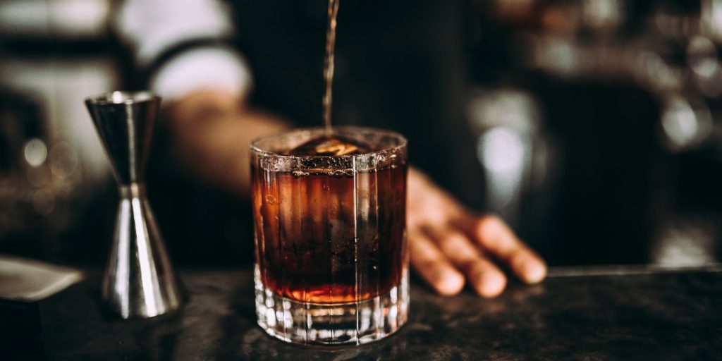 A close up shot of a barman pouring a bourbon into a rocks glass with ice.