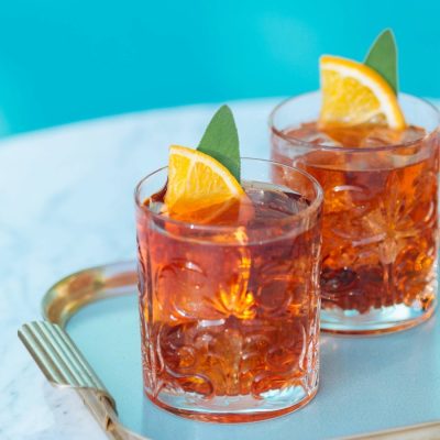 Two Negroni cocktails on a glass tray surrounded by snacks