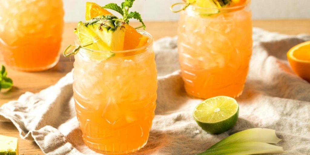 Close up image of a trio oif Aperol Bird of Paradise Cocktails garnished with fresh pineapple and mint, presented on a table partially covered in white linen