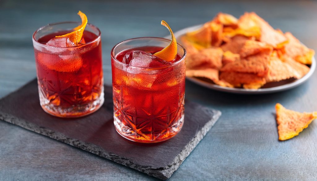 Two Rosita cocktails with orange peel garnish served with nachos