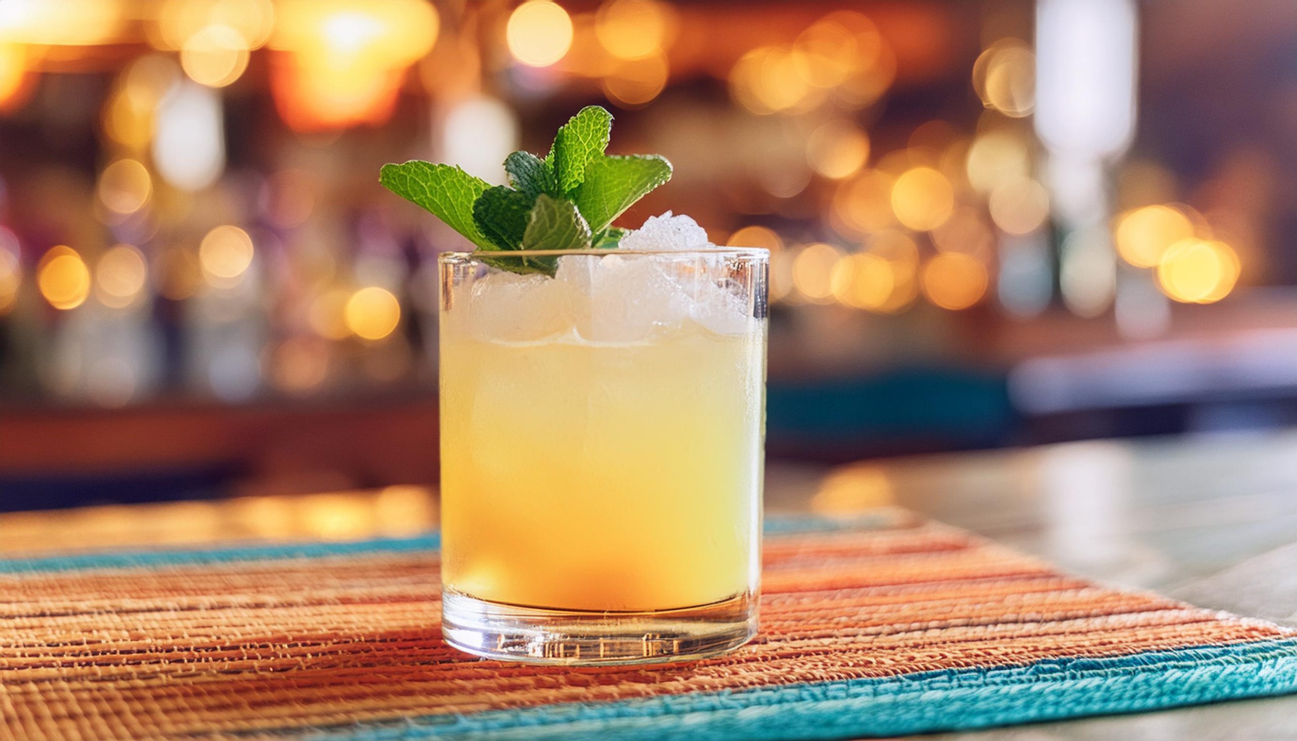 An Anejo Smash tequila cocktail served in a lowball glass on crushed ice, garnished with a fresh sprig of mint