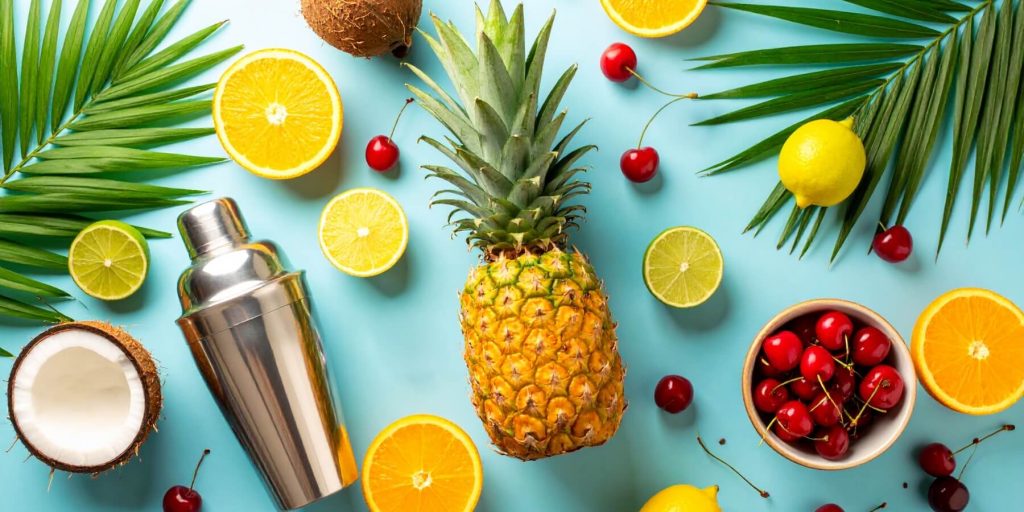 Flat lay of different ingredients used to make the best tropical drinks including pineapple, limes, oranges, coconut and cherries