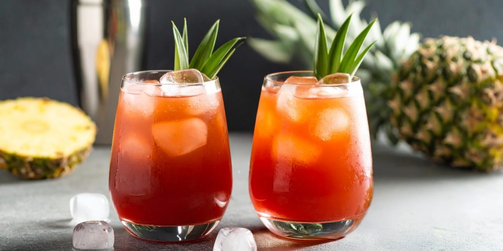 Two reddish amber Jungle Bird cocktails with pineapple frond garnish 
