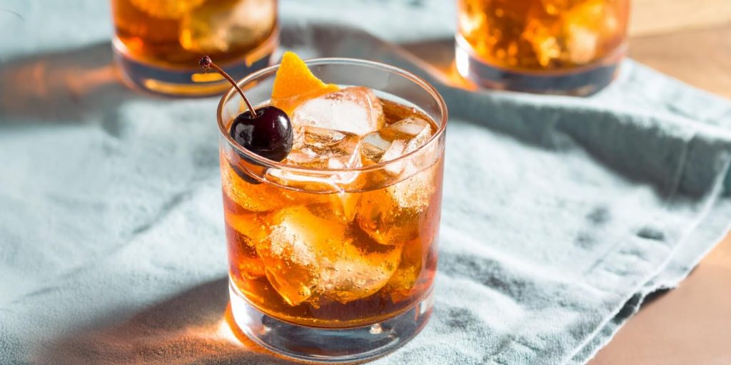 Three Maple Old Fashioned cocktails on a blue cltoh on a brown table