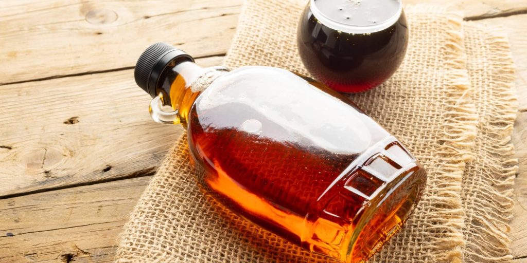 A bottle of maple syrup lying on a burlap sack on top of a scrubbed wood table