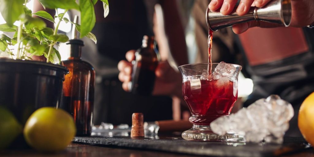 A close up shot of a home bartender pouring Campari into a glass with ice
