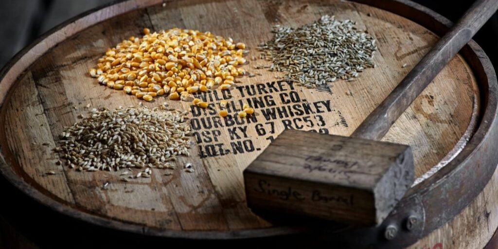 The top of a Wild Turkey bourbon barrel with piles of corn, wheat and rye grains with a wooden mallet