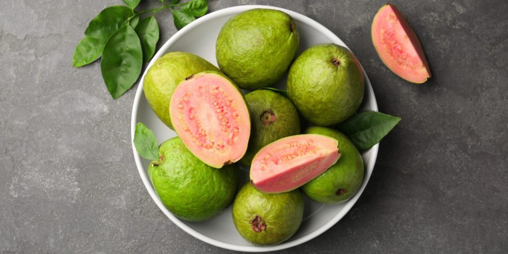 A bowl of guava fruit with sliced pieces on a dark surface.