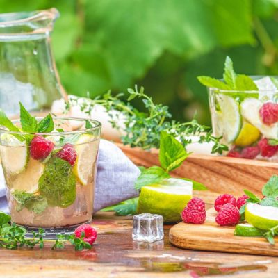 A summer table cocktail set up with a jug of cocktails and several glasses filled with fruity cocktails.