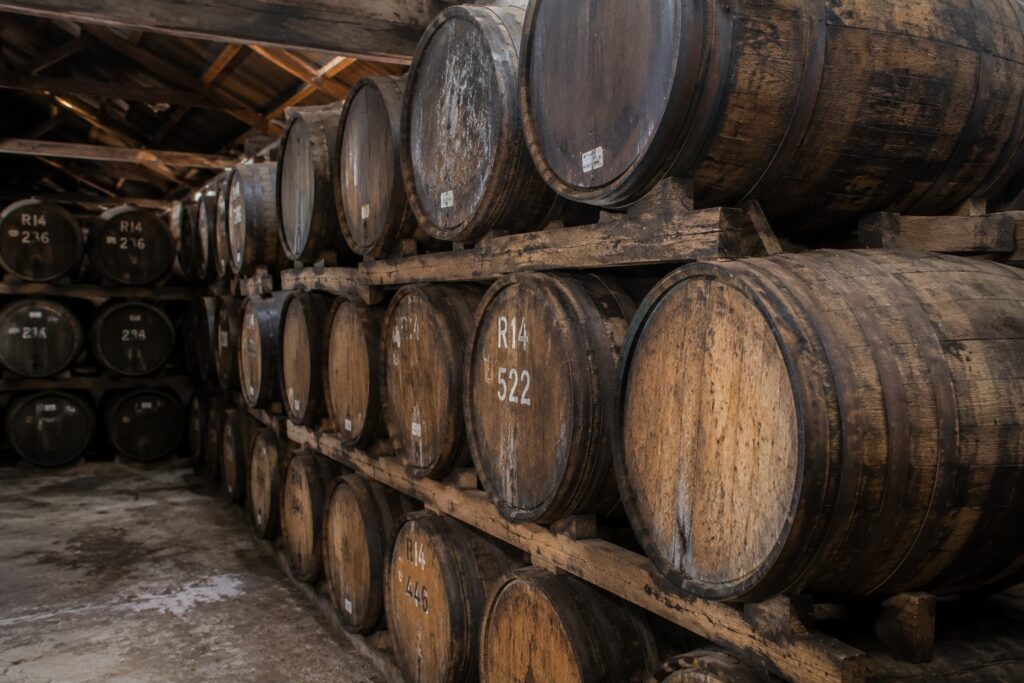 Rows of weathered oak barrels stacked inside a traditional rum ageing warehouse.